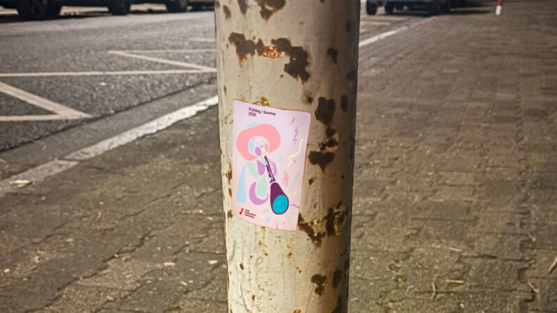Aufkleber mit dem Motiv Frühling/Sommer 2025 auf einem rostigen Poller am Straßenrand